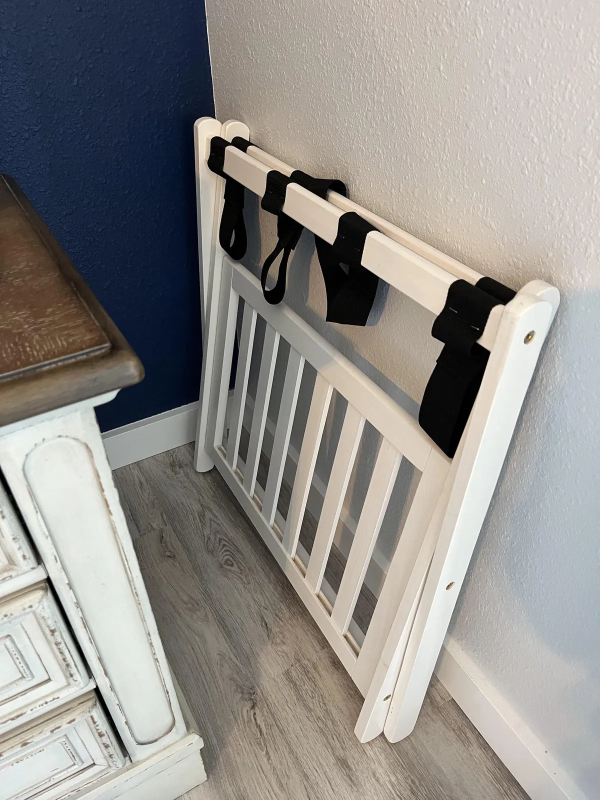 A white safety gate set against a dark blue wall, adjacent to a wooden dresser, creates a safe and nurturing corner ideal for young children. The overall vibe is one of security and family-friendliness, reinforcing peace of mind for families.