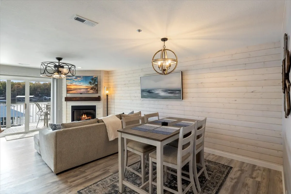 An open-concept living and dining area with large windows offering scenic views, a comfortable dining table, cozy sofa, and a fireplace. Artwork and décor create a relaxed, inviting vibe ideal for gathering after a day of exploring.