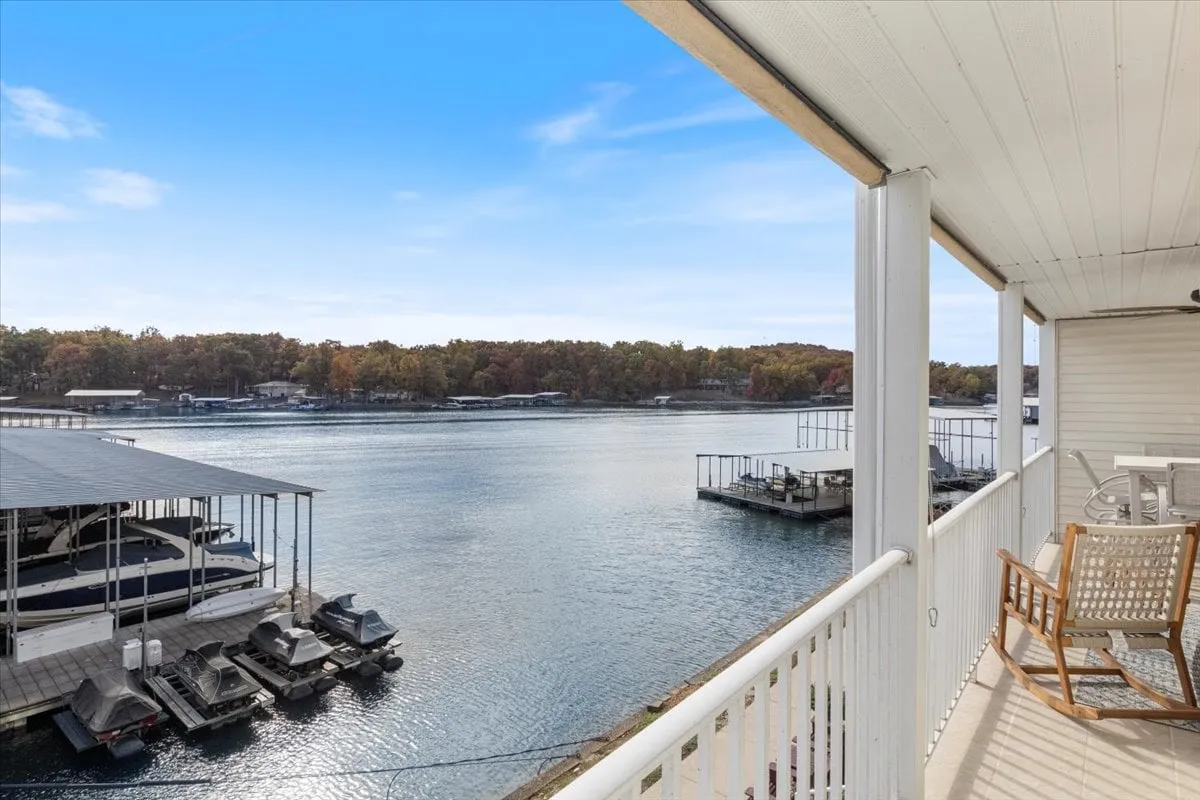 This image features a peaceful lake view with a dock area and several boats moored nearby. The scene suggests easy access to lake activities such as boating and fishing, and the porch area hints at a comfortable spot for families to relax and take in the scenery.