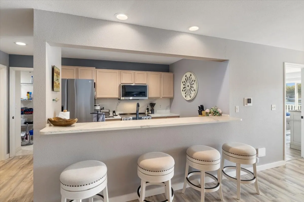 A bright and welcoming kitchen with a spacious island and bar seating, complemented by modern appliances and a decorative wall piece. The layout hints at easy meal prep and socializing, with natural light streaming in from nearby windows.