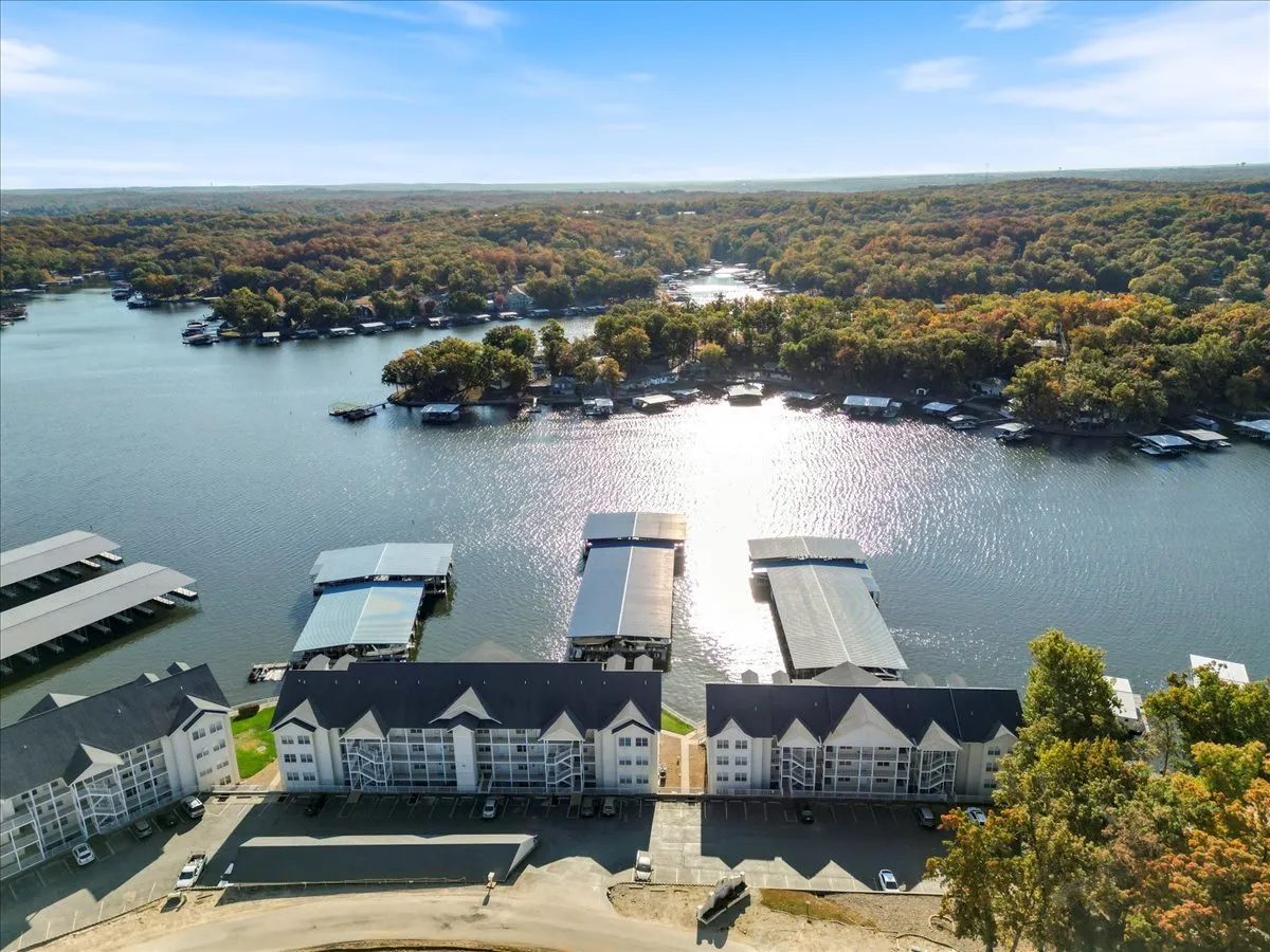 A wide view of the lake with visible marinas, autumn foliage, and a residential building. The panoramic scene captures the broader natural and recreational context, inviting exploration and alluding to the destination’s popularity for boating, fishing, and lakeside leisure.