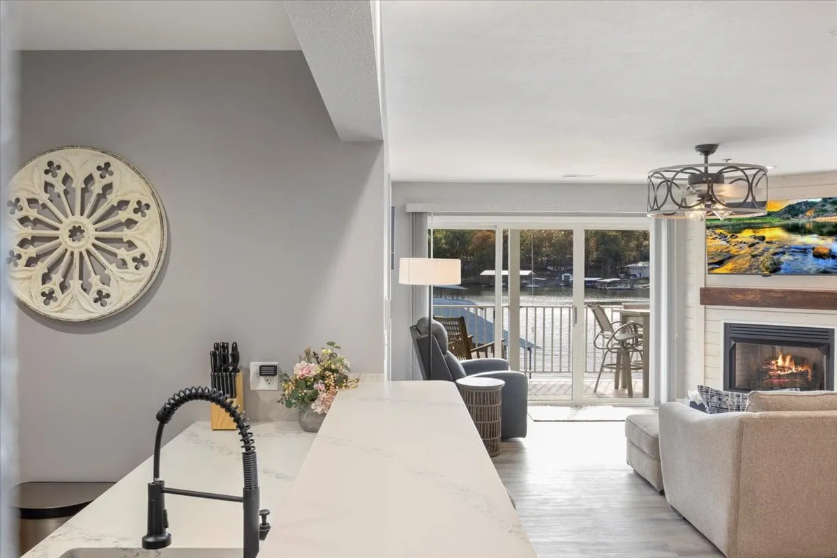 A modern kitchen island paired with a fireplace and large windows that reveal a beautiful lakefront view. The area feels both luxurious and homey, suggesting tranquility and easy access to the outdoors.
