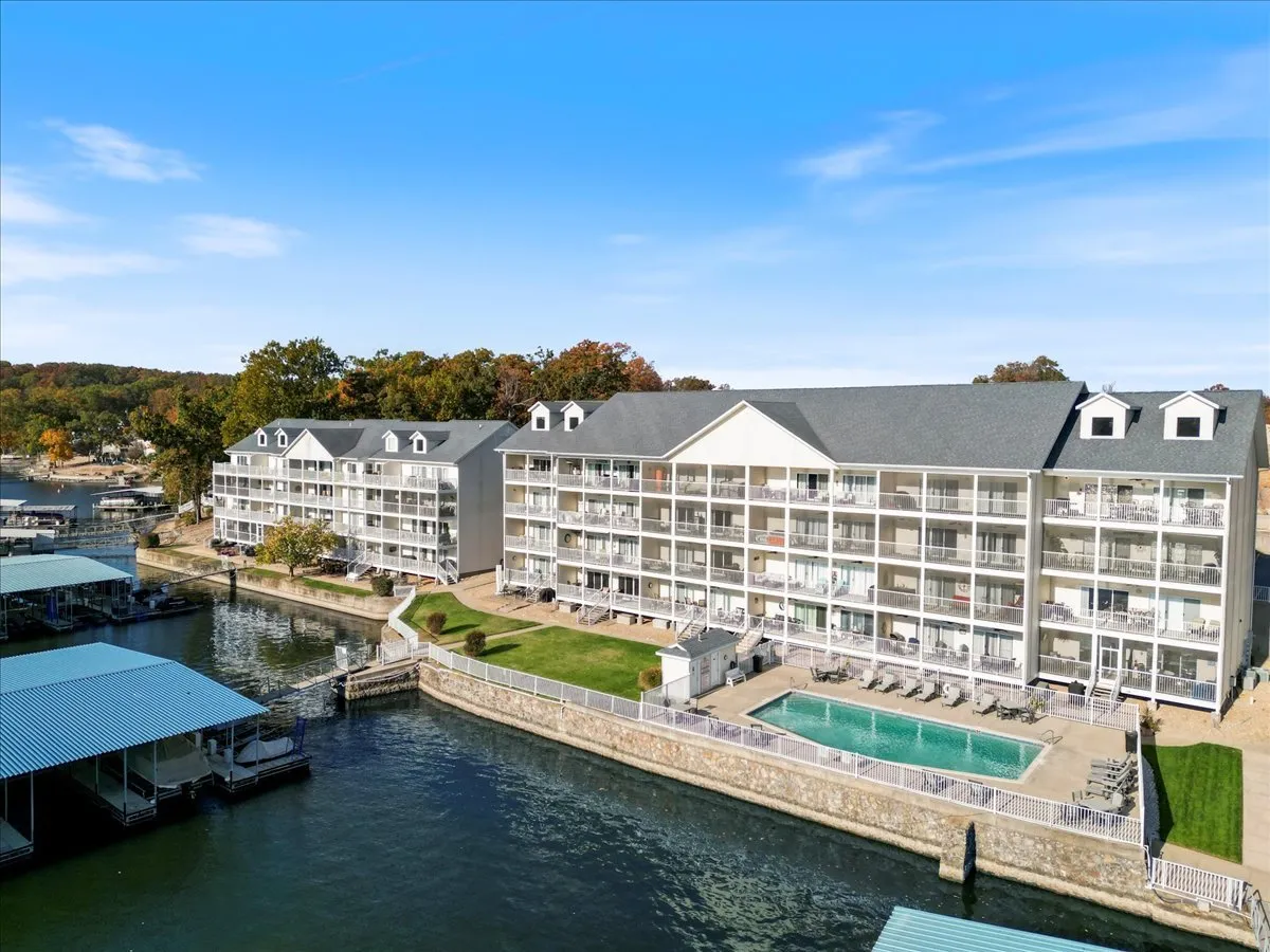 A vibrant exterior scene showcasing a swimming pool by the lake, surrounded by balconies and lush greenery. The pool area is inviting for both kids and parents, offering views of the waterfront and space for social gatherings or family fun.