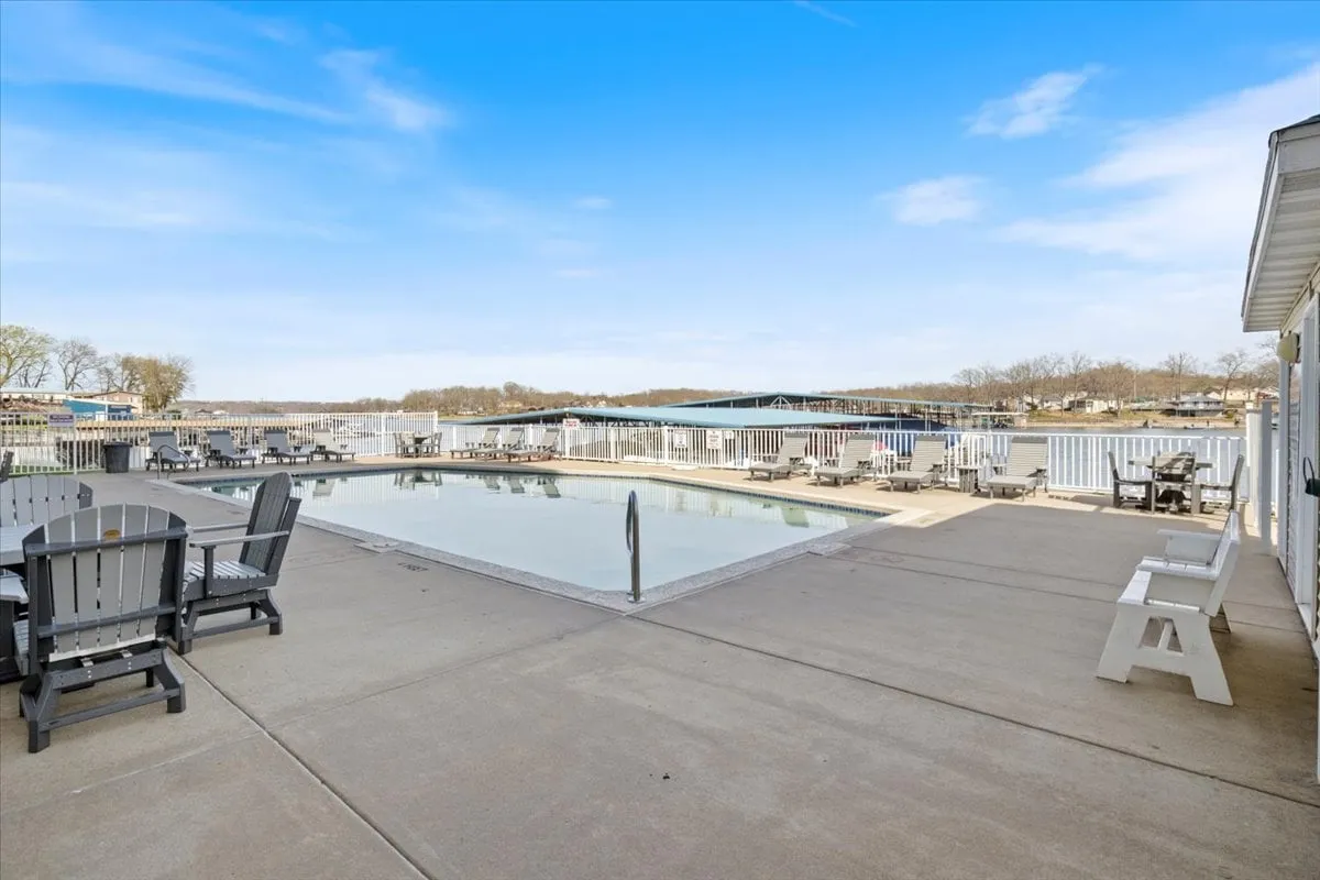 A wide-angle exterior image capturing the swimming pool, dock, and adjacent seating area. The view highlights the seamless connection between poolside leisure and access to the community dock and boat slip, with the water and boats in clear view.