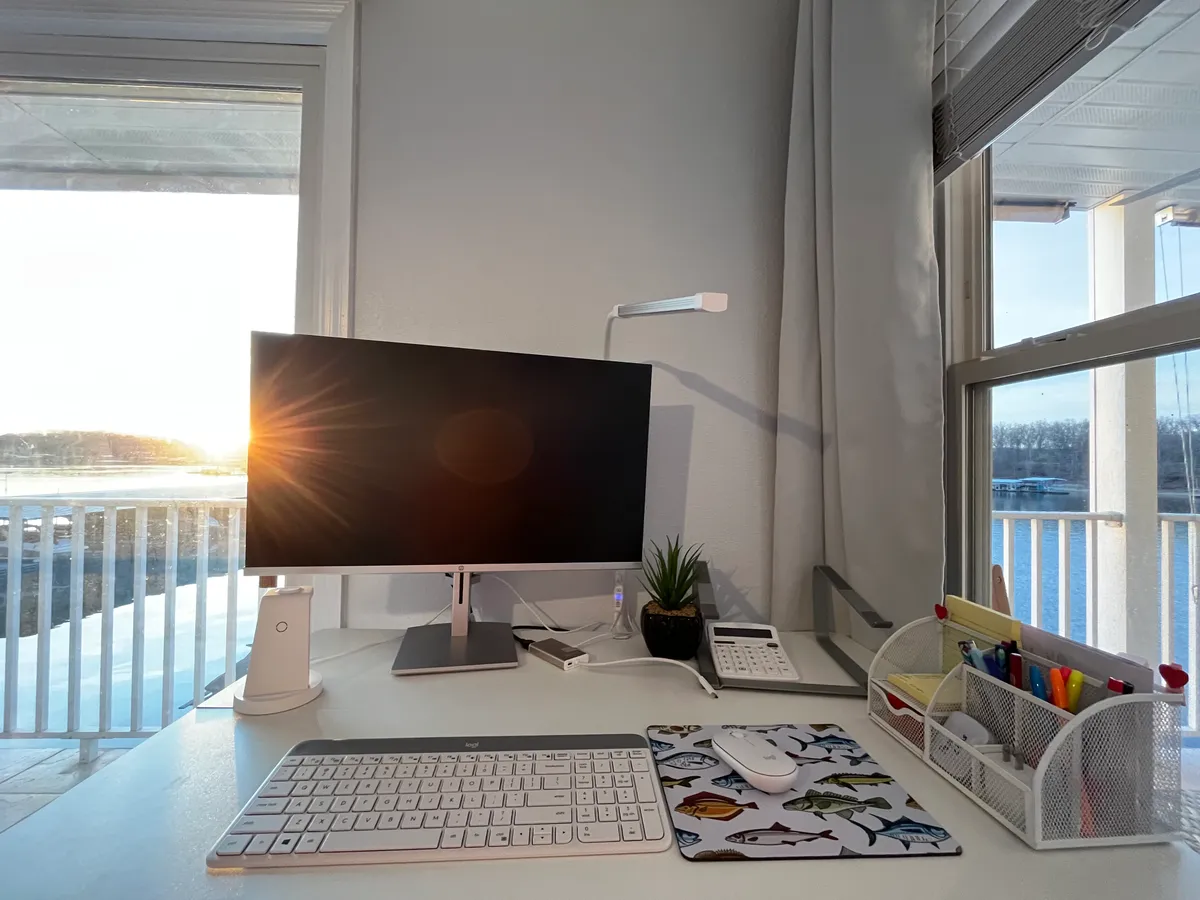 A sleek workspace is set up with a computer monitor, desk accessories, and a window offering a tranquil view. The scene is bathed in soft natural light, creating an inviting atmosphere for productivity. The workspace exudes a sense of focus and tranquility, perfectly suited for remote work.